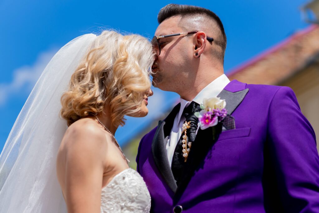 A romantic wedding moment captured with the couple sharing a tender kiss under a clear blue sky.